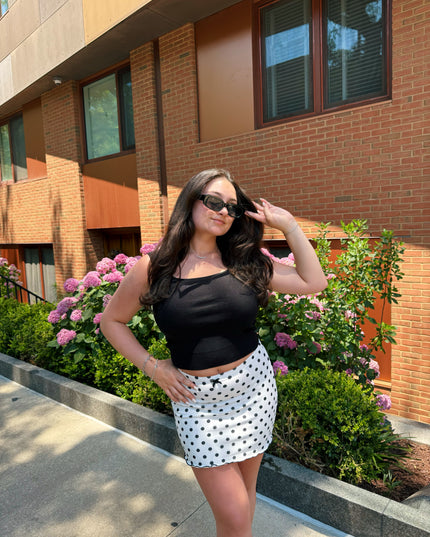 Woman posing outdoors in front of a brick building with pink flowers.