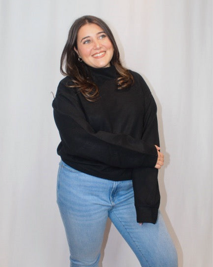 Person wearing a black sweater and blue jeans against a plain background