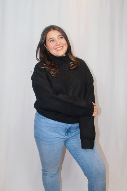Person wearing a black sweater and blue jeans against a plain background