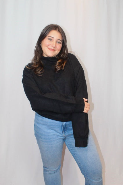 Person wearing a black sweater and blue jeans against a plain background