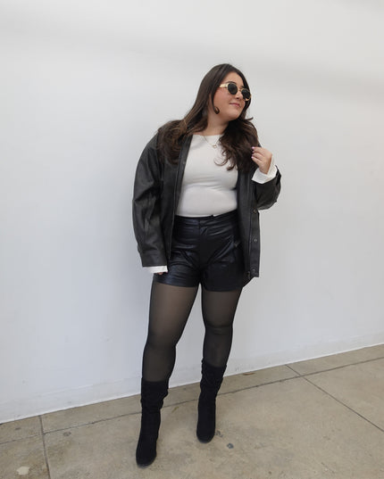 Person wearing a black leather jacket, white shirt, and black stockings on a white background