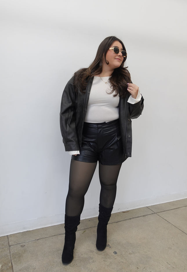 Person wearing a black leather jacket, white shirt, and black stockings on a white background