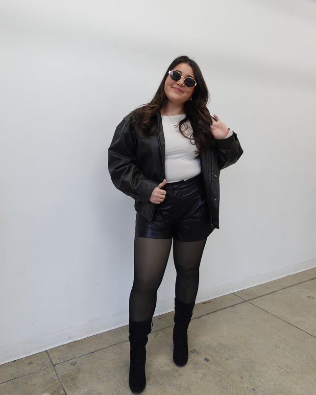 Person wearing a black outfit with sunglasses on a white floor.