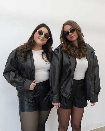 Two women wearing matching black leather jackets and shorts against a white background