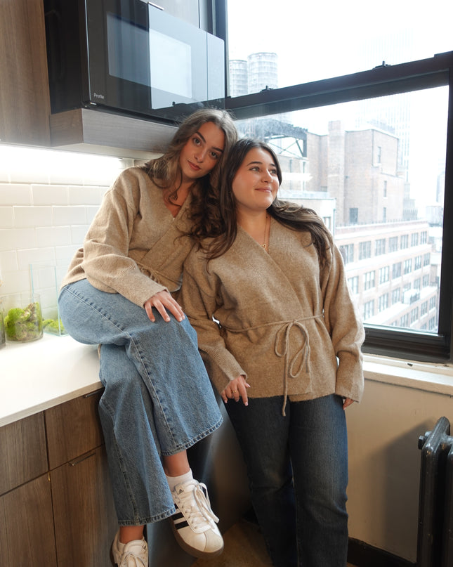 Two women taking a mirror selfie indoors with a cityscape view outside.