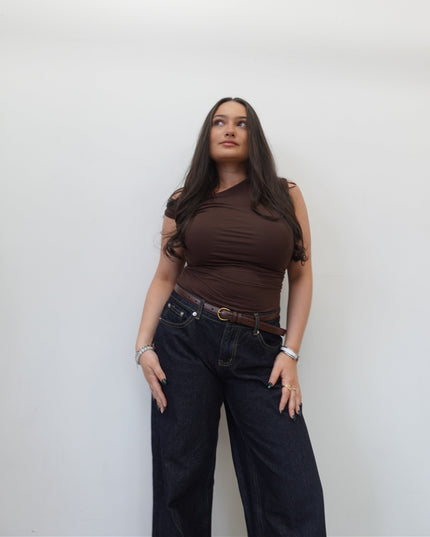 Woman wearing a brown top and dark jeans against a white background