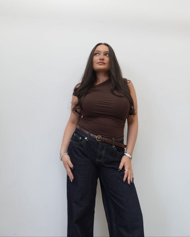 Woman wearing a brown top and dark jeans against a white background