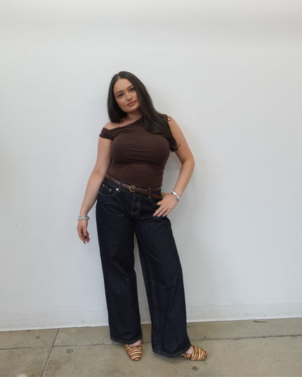Woman in brown top and dark pants standing on a white floor.