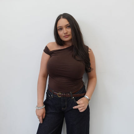 Woman in a brown top and black pants standing against a white background
