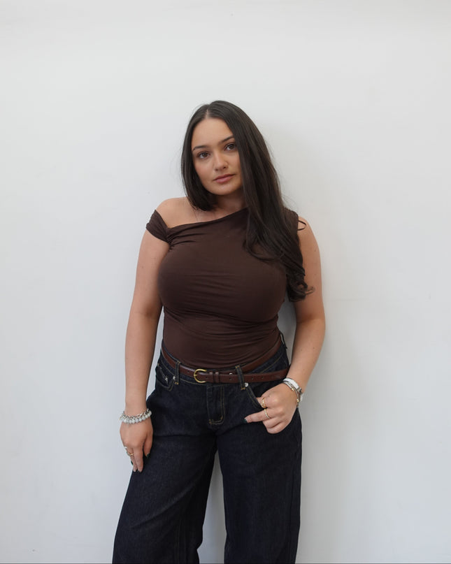 Woman in a brown top and black pants standing against a white background
