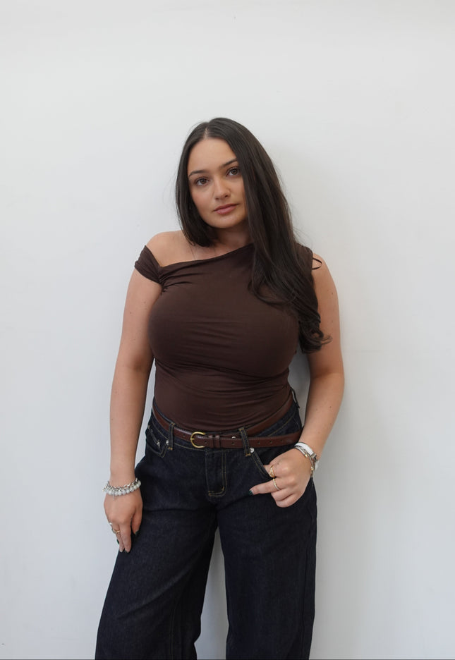 Woman in a brown top and black pants standing against a white background