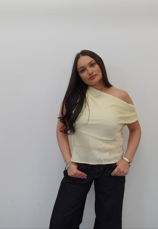 Woman wearing a light-colored top and dark pants on a plain background