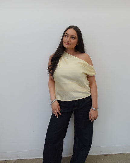 Woman in a yellow top and black pants standing against a white wall